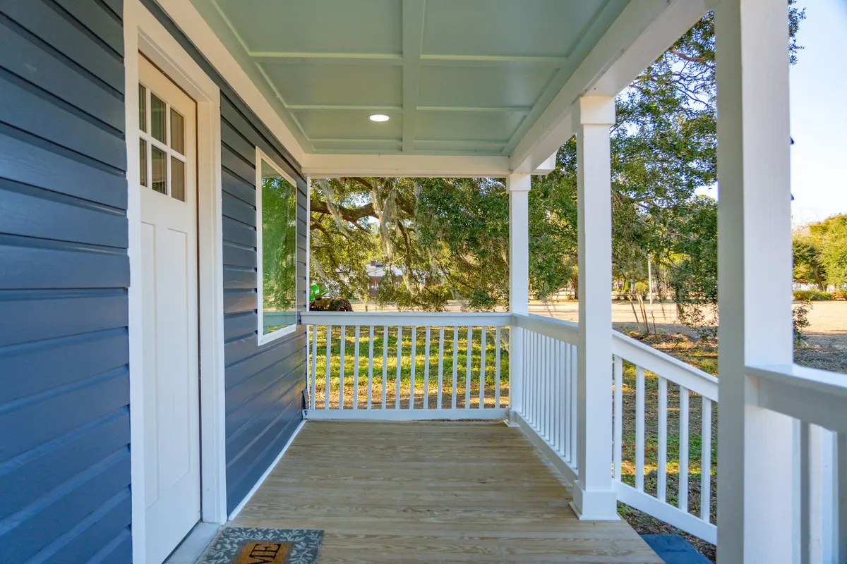 This image showcases the front door of the home, framed by white railings, blue siding, and inviting wooden porch flooring. Sunlight streams in, highlighting an atmosphere perfect for greeting friends or coming together after a day of local adventures.