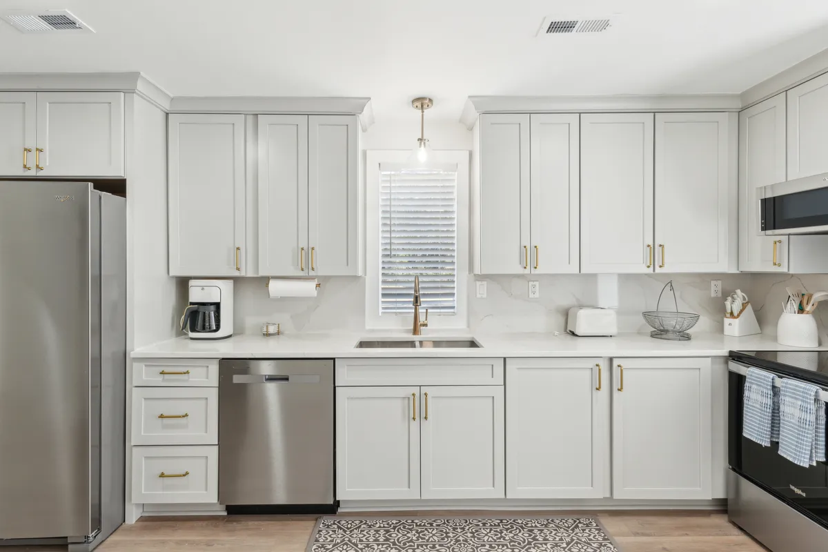 A bright kitchen scene featuring a wide sink, stainless steel appliances, expansive countertops, and a window that lets in natural light. The arrangement suggests a functional space ideal for both meal preparation and group activities.