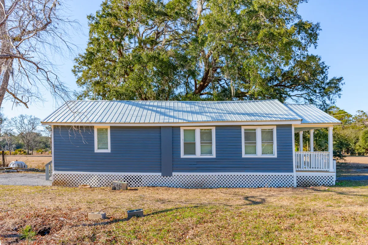 This image showcases the blue exterior of the home with a charming white porch railing and a large tree in the background. The porch and open setting evoke a sense of outdoor leisure and connection to nature, inviting families to relax and unwind after a day at the beach or exploring nearby natural attractions.