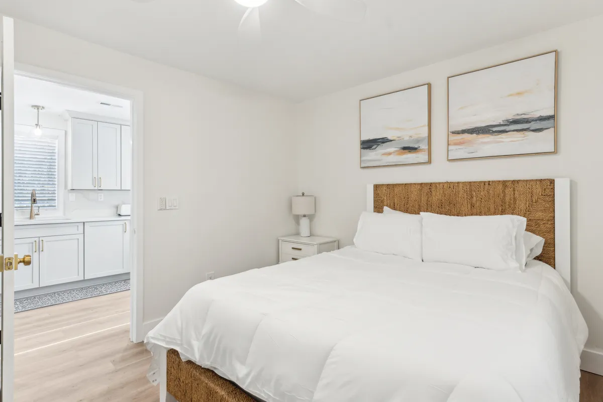 A serene bedroom scene featuring a neatly made bed with soft linens, a calming artwork above the headboard, and a nightstand with a warm-lit lamp. The atmosphere is peaceful and inviting, suggesting a perfect space for relaxation and restful sleep.