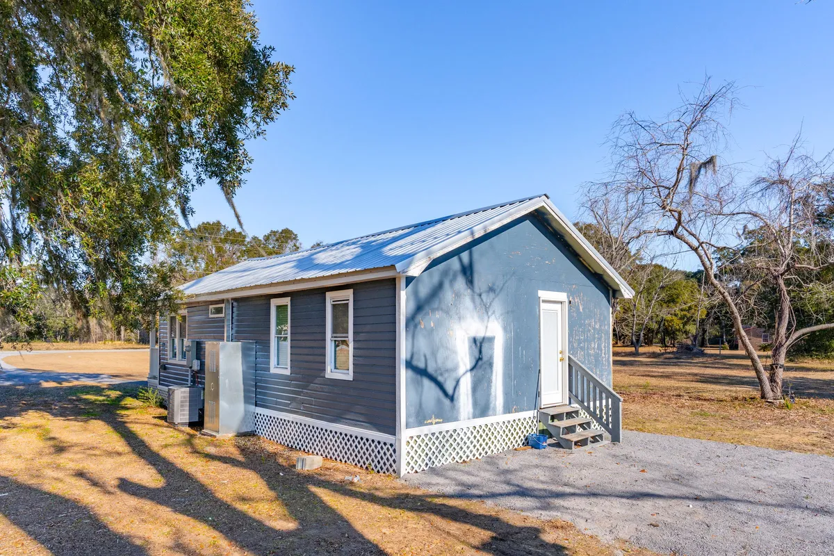 This exterior shot features the blue house with steps leading to the entrance, surrounded by mature trees. The spacious yard and tranquil atmosphere invite thoughts of outdoor games, family picnics, and peaceful mornings, which align with the section's mention of evening games and safe, scenic outdoor spaces.
