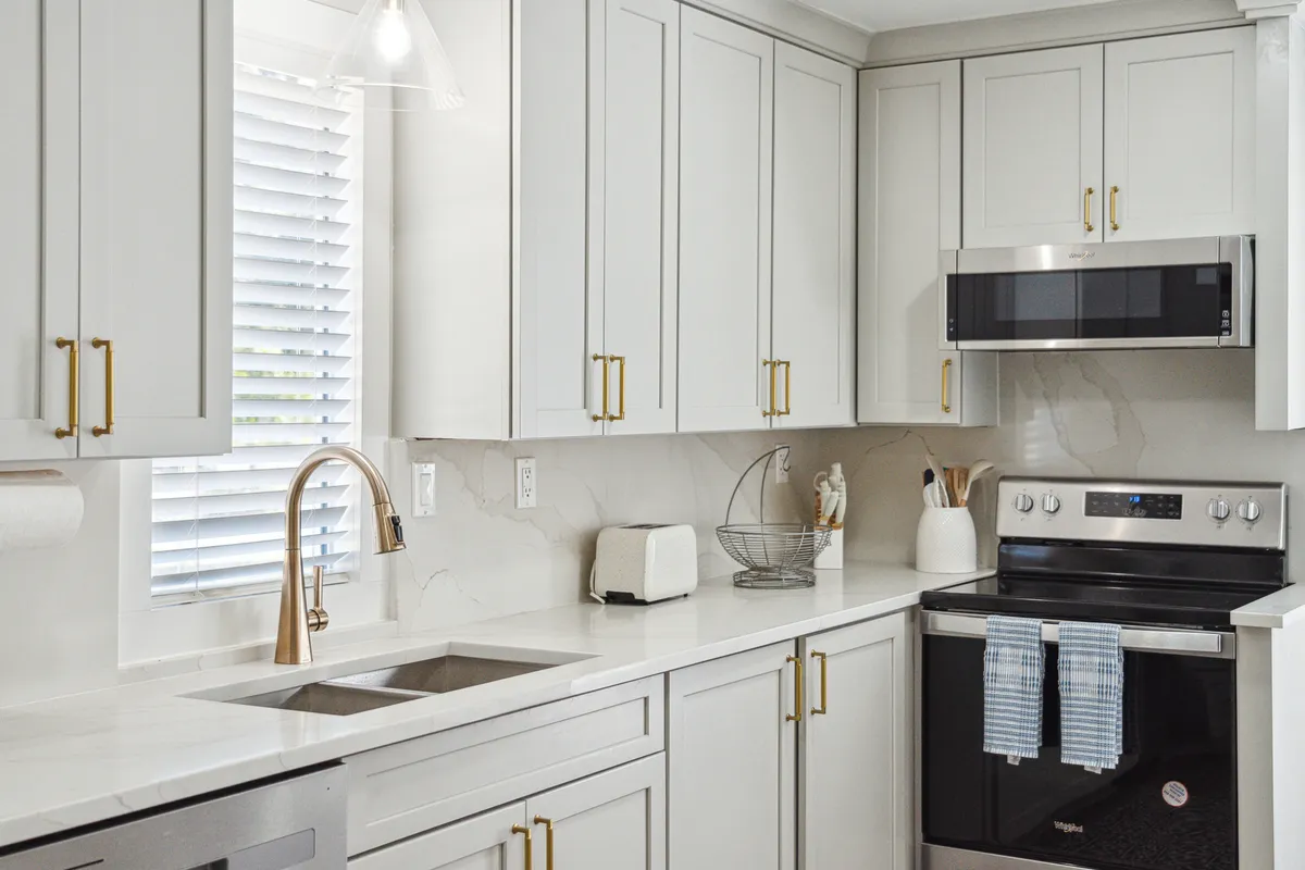 A modern kitchen with stainless steel appliances, crisp white cabinetry, gold hardware, and a wide countertop area. The setting is both chic and cozy, suggesting a space equally suited for family breakfasts or elegant dinners.
