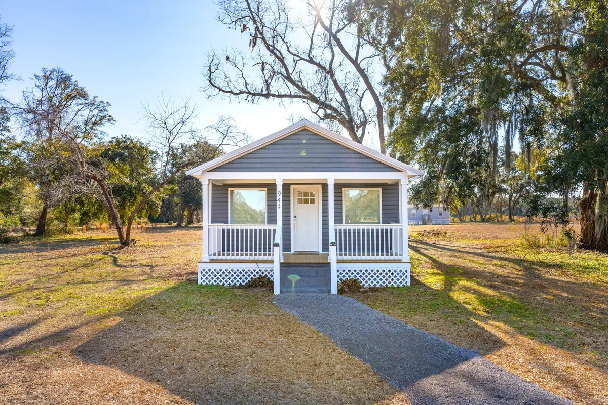 This image features the front porch with steps leading to the door, large windows, and a lush backdrop of trees. The porch is styled for relaxation, perfect for enjoying coffee, reading, or gathering with family. The scene exudes peacefulness and the beauty of outdoor living.
