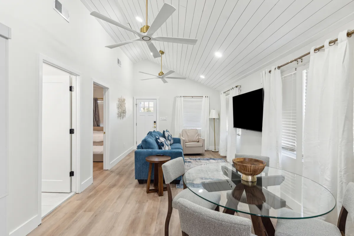 The hero image showcases a bright, inviting living and dining area featuring a plush blue sofa, a stylish glass dining table, airy curtains, and a large ceiling fan. The space radiates comfort and warmth, perfect for relaxing or sharing meals with family and friends.