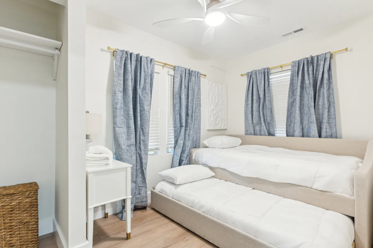A cozy bedroom with a bunk bed dressed in soft bedding, blue curtains providing privacy, and a nightstand with a reading lamp. The space feels inviting for families or friends, offering a sense of shared comfort and tranquility.